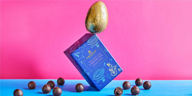 Chocolate Easter egg atop a blue box surrounded by chocolate truffles.